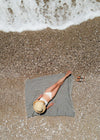 Aligned Bezzazan Turkish beach towel, black and white oversized, with tassels, model is tanning on top at the beach by sea