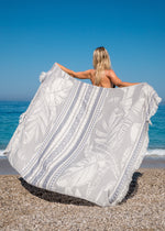 Oversized Turkish Towel Flourishing XL by Bezzazan, with breezy boho tropical design of palm trees, held by blonde girl at beach