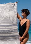 oversized Flourishing XL lightweight Turkish Towel by Bezzazan with palms, held by happy boho girl sunglasses and swimsuit