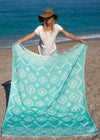boho girl holds sandfree eco-friendly Turkish towel with tribal design in turquoise color at beach in boho hat white shirt