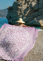 Oversized Turkish towel in amethyst color simple mandala design with tassels, Passionate Bezzazan held by model on beach