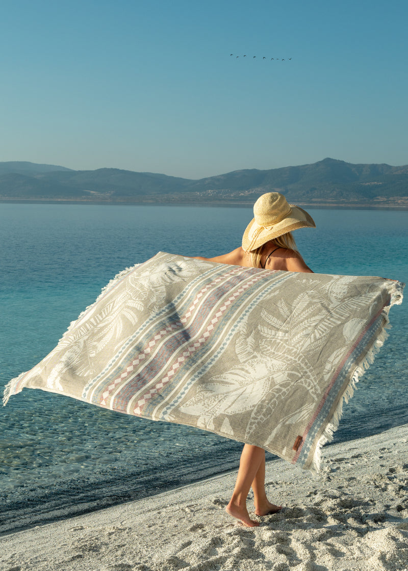 Flourishing Oversized Luxury Turkish Towel Bezzazan, held by girl in boho straw hat on turquoise water white sand beach 