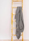 Stylish and sustainable Aligned Throw Blanket by Bezzazan, oversized black and white with tassels, styled on a yellow ladder